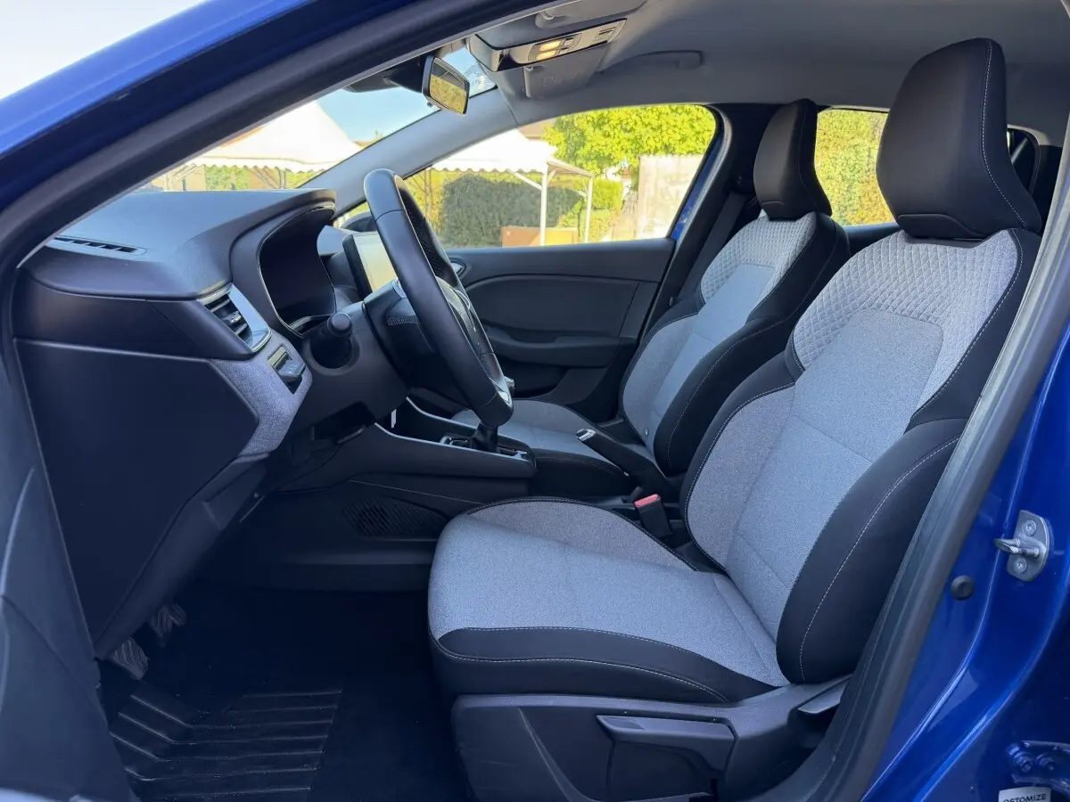 Vue intérieure côté conducteur de la Renault Clio Evolution TCe 90 2024 bleu, sièges tissu gris et noir, volant multifonctions.