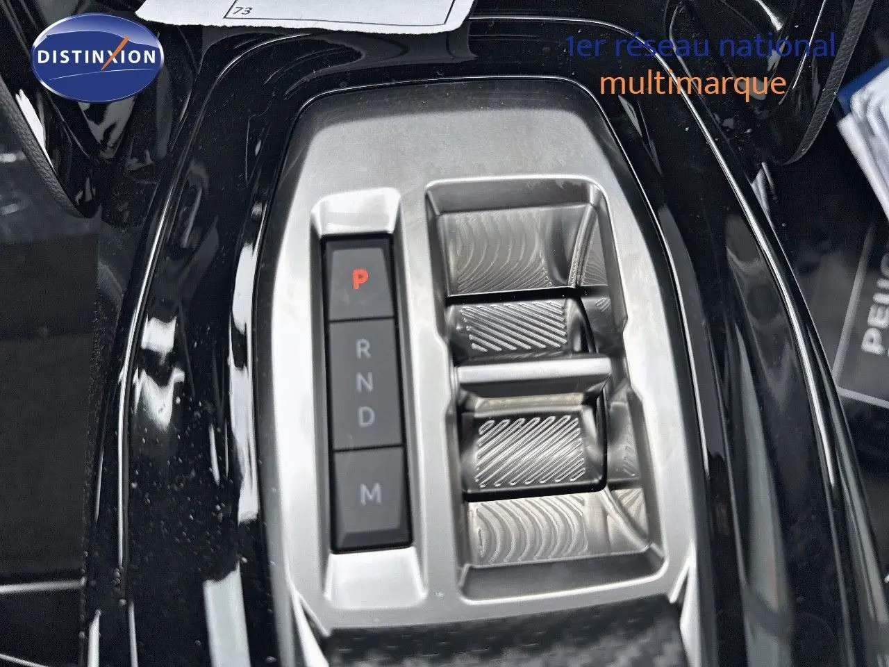 Gros plan sur la console centrale noire métallisée du Peugeot 2008 Hybrid avec sélecteur de boîte automatique et boutons de vitesses.