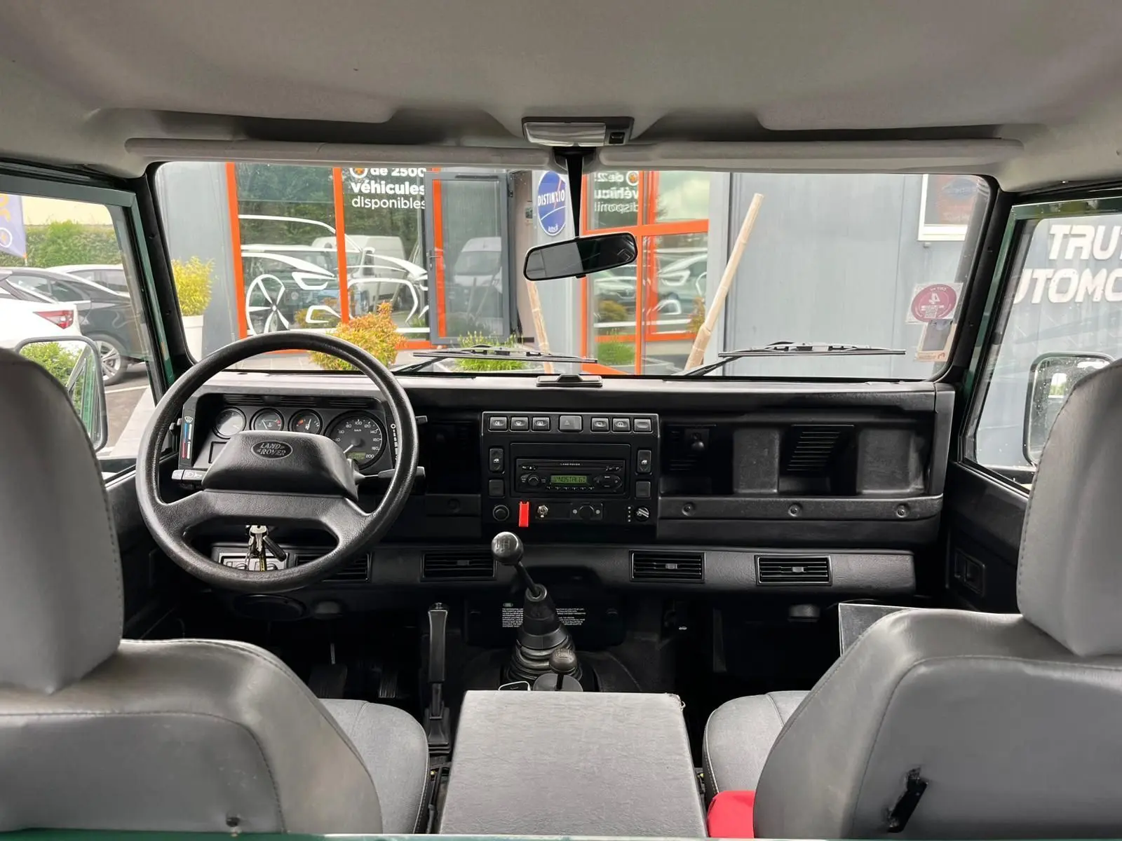 Vue intérieure avant du Land Rover Defender 90 Hard Top 2004, tableau de bord noir avec volant et levier de vitesses manuelle visibles.