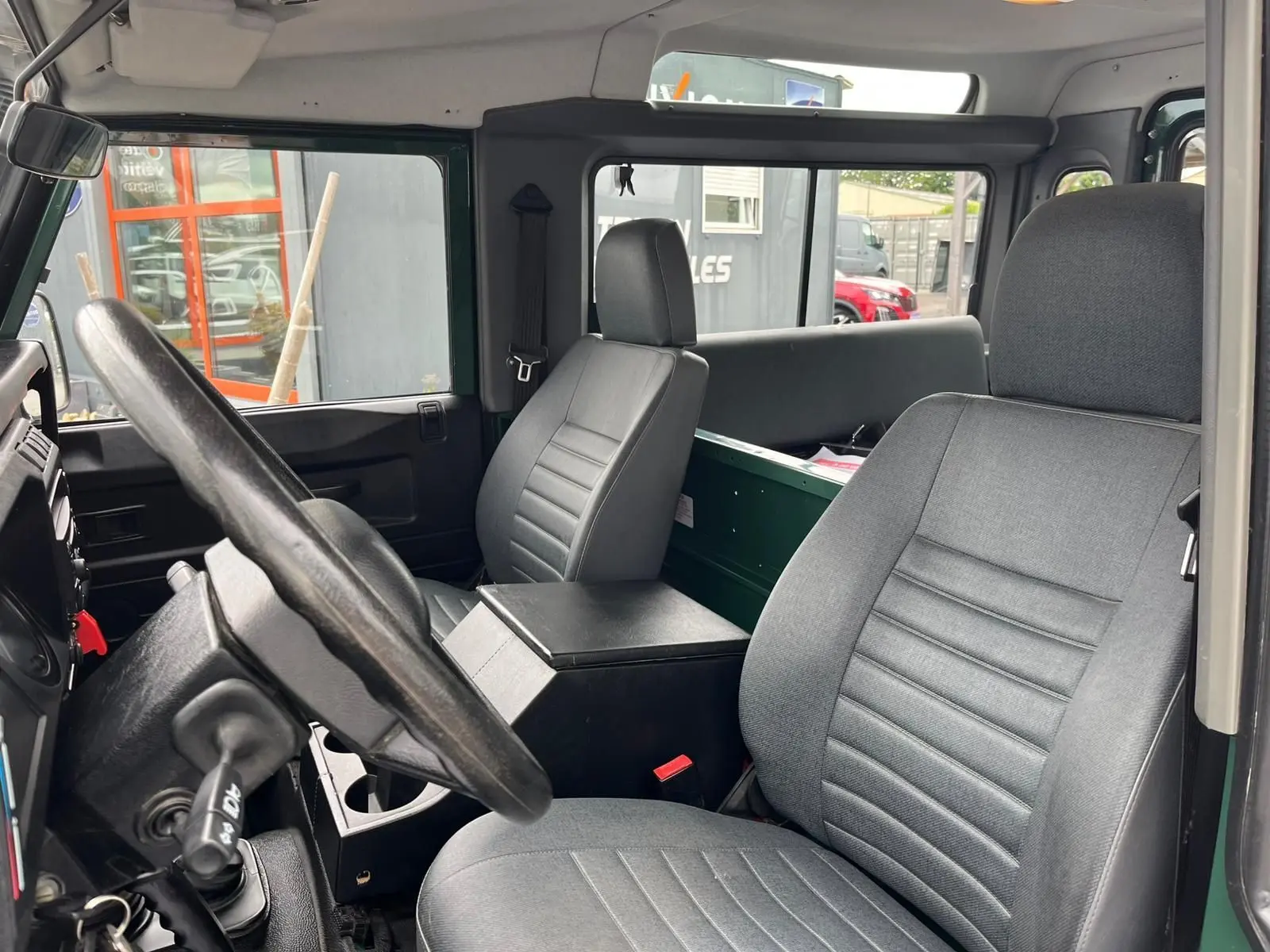 Intérieur du Land Rover Defender 90 Hard Top vert, vue côté conducteur avec sièges gris et tableau de bord simple.