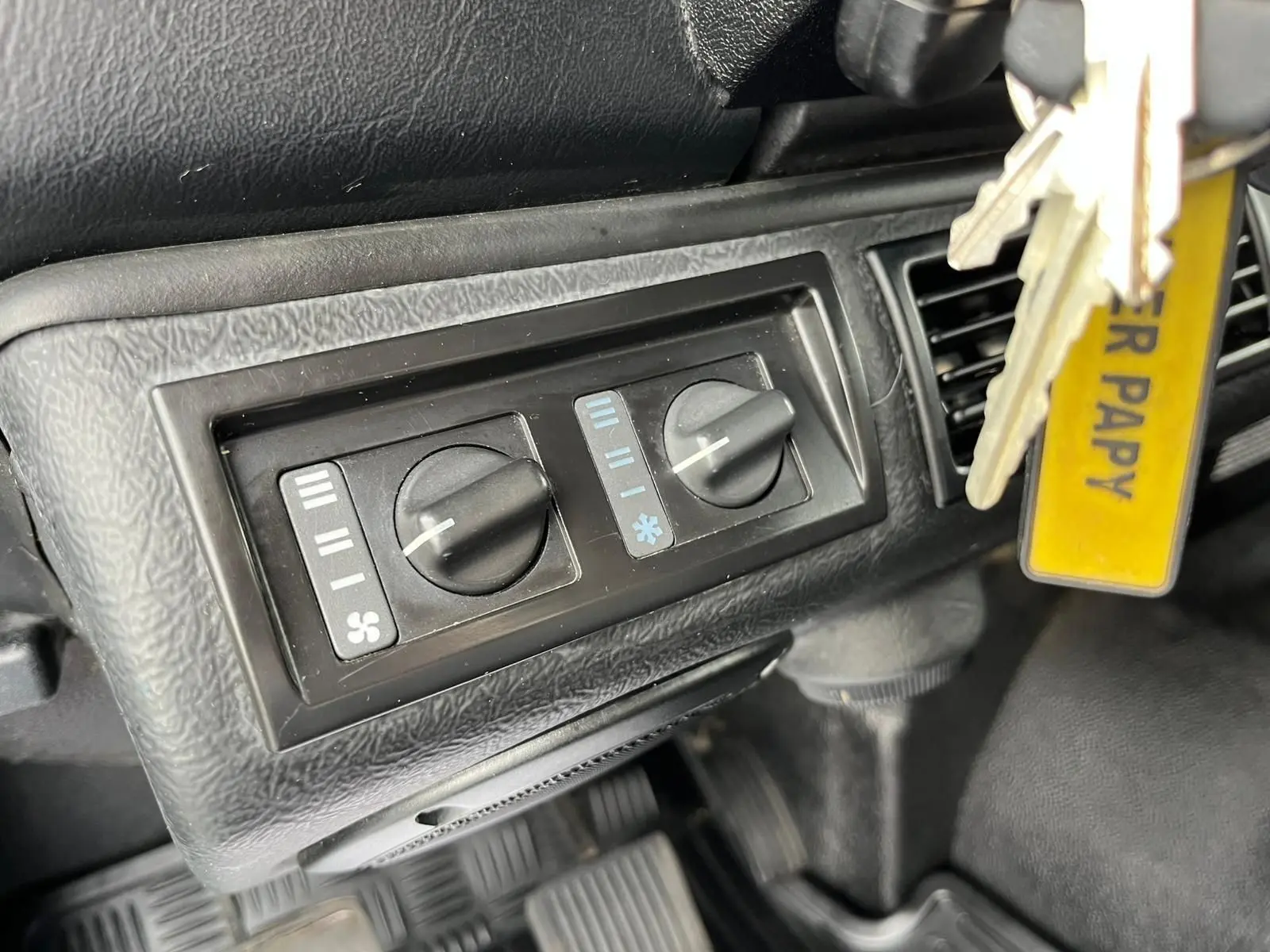 Gros plan sur les commandes de ventilation noires du tableau de bord du Land Rover Defender 90 vert de 2004.