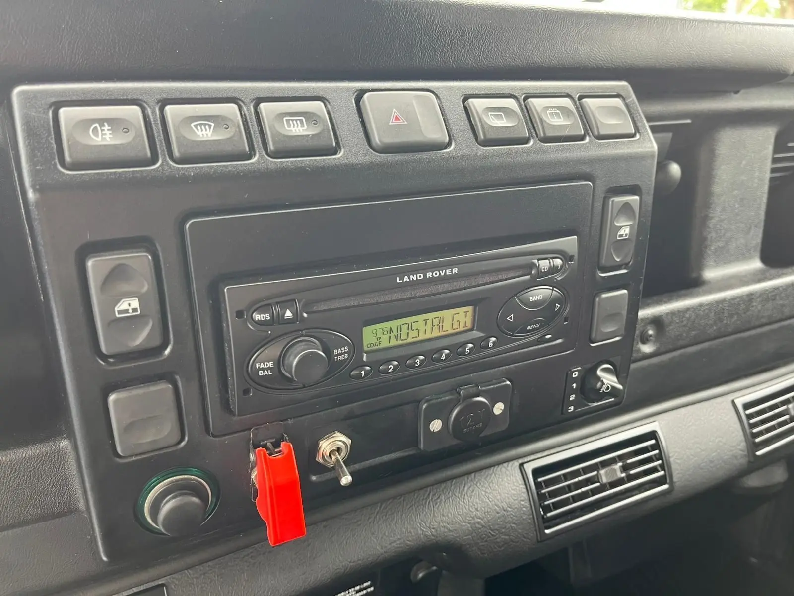 Tableau de bord noir du Land Rover Defender 90 Hard Top 2004 avec autoradio d'origine et interrupteurs alignés.