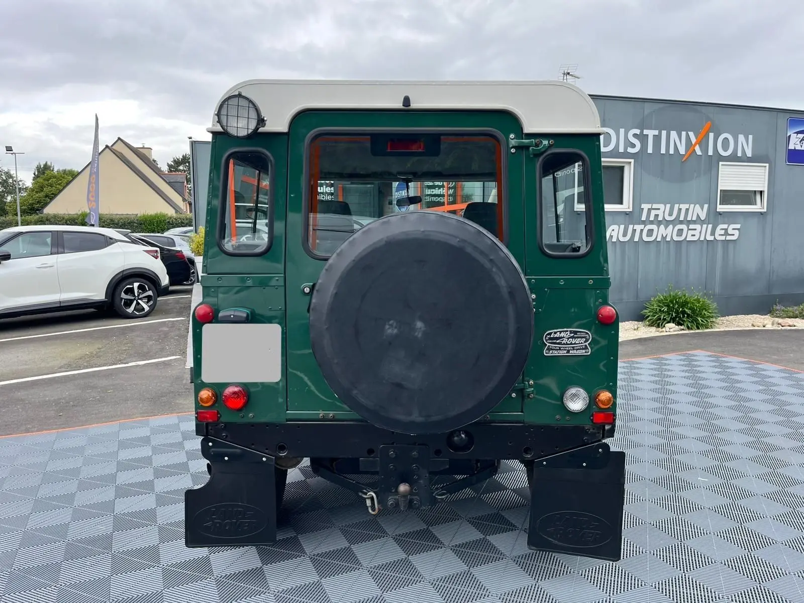 Vue arrière d'un Land Rover Defender 90 vert 2004 avec roue de secours et Hard Top blanc visible.