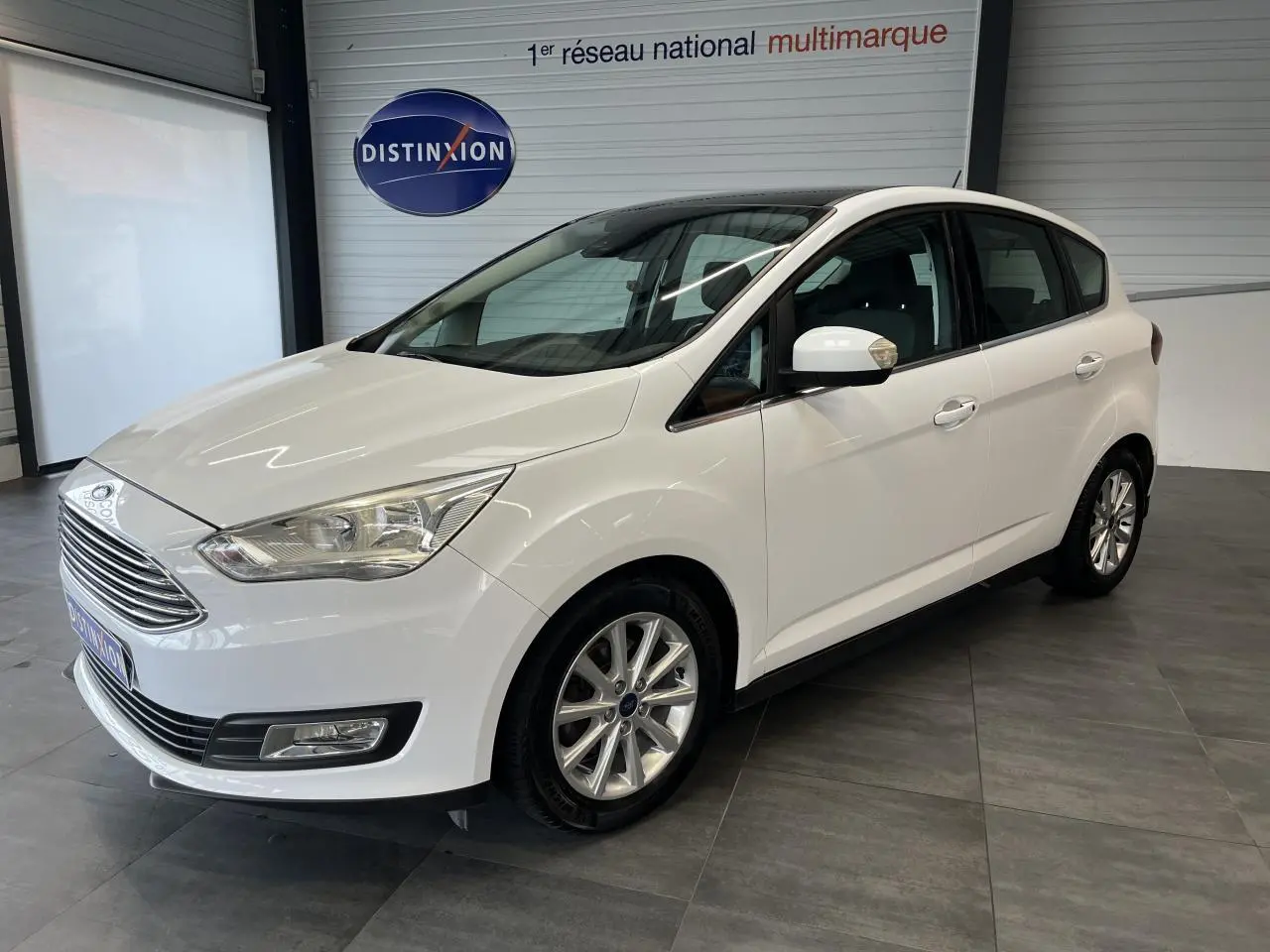 Ford C-MAX blanc en vue 3/4 avant droit, avec jantes alliage 16 pouces et toit panoramique visible.