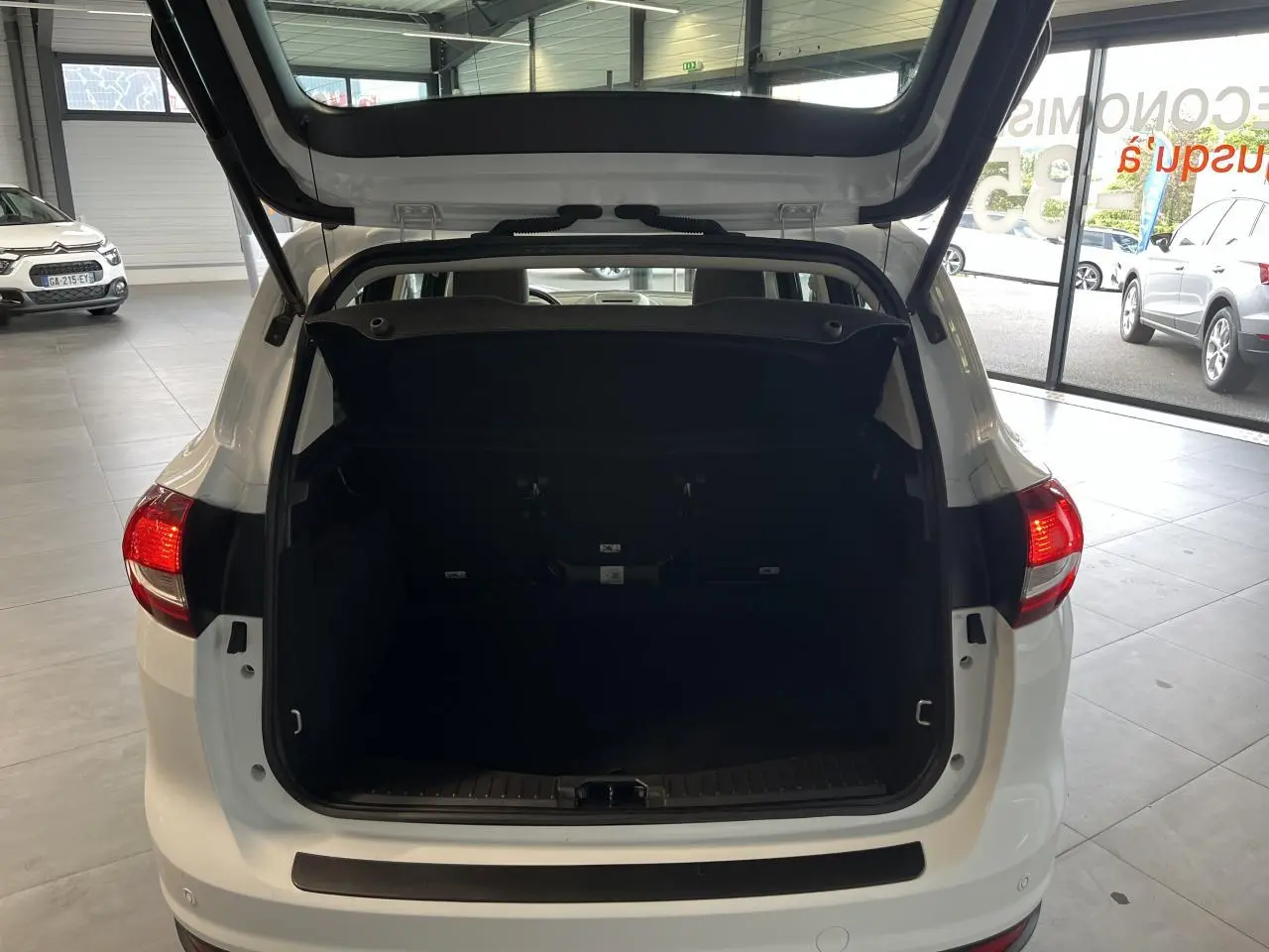 Vue arrière ouverte du coffre d'un Ford C-MAX blanc 2018 en intérieur, montrant l'espace de chargement vide.