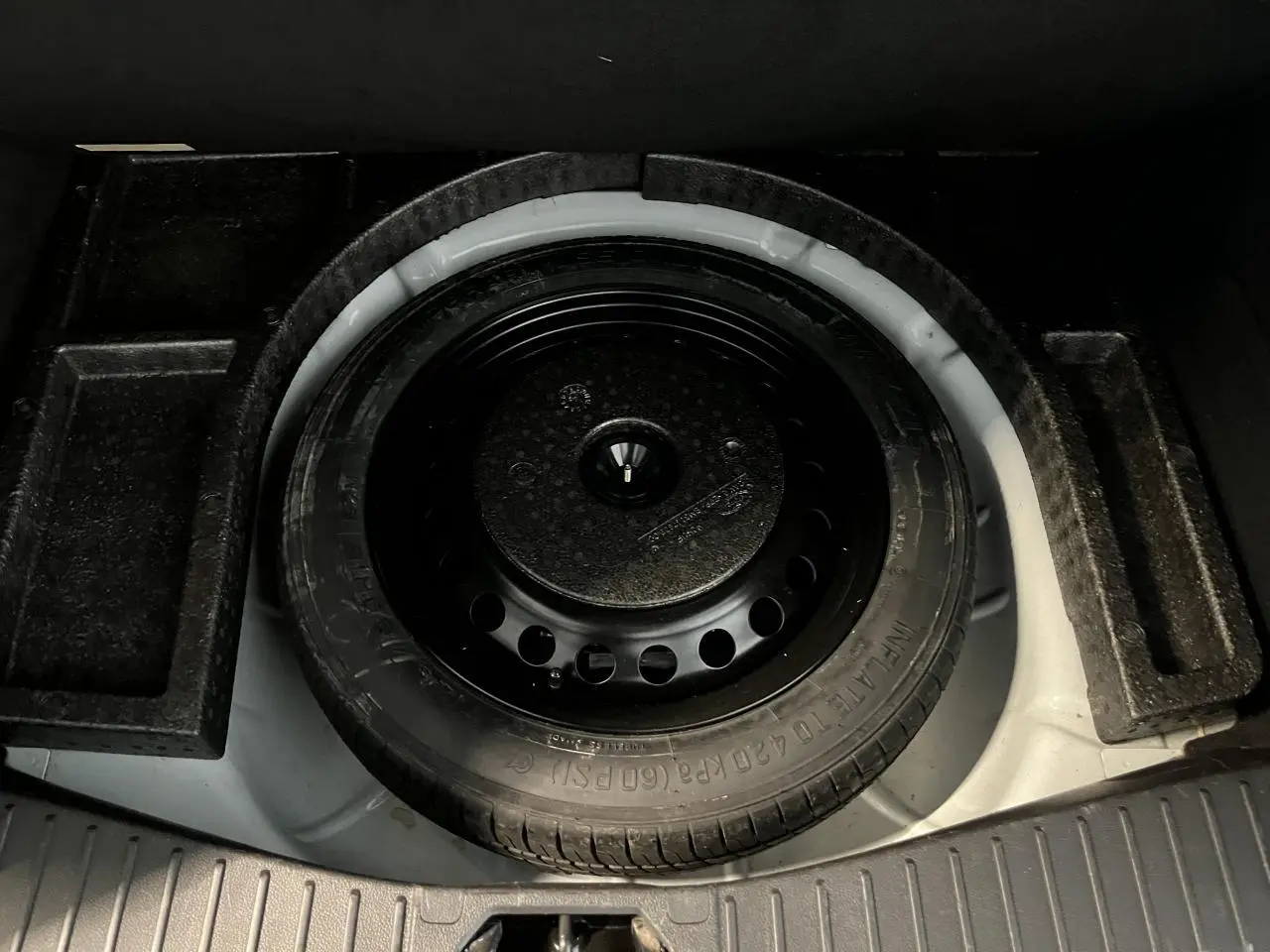 Gros plan sur la roue de secours galette noire dans le coffre blanc d'une Ford C-MAX Titanium 2018.