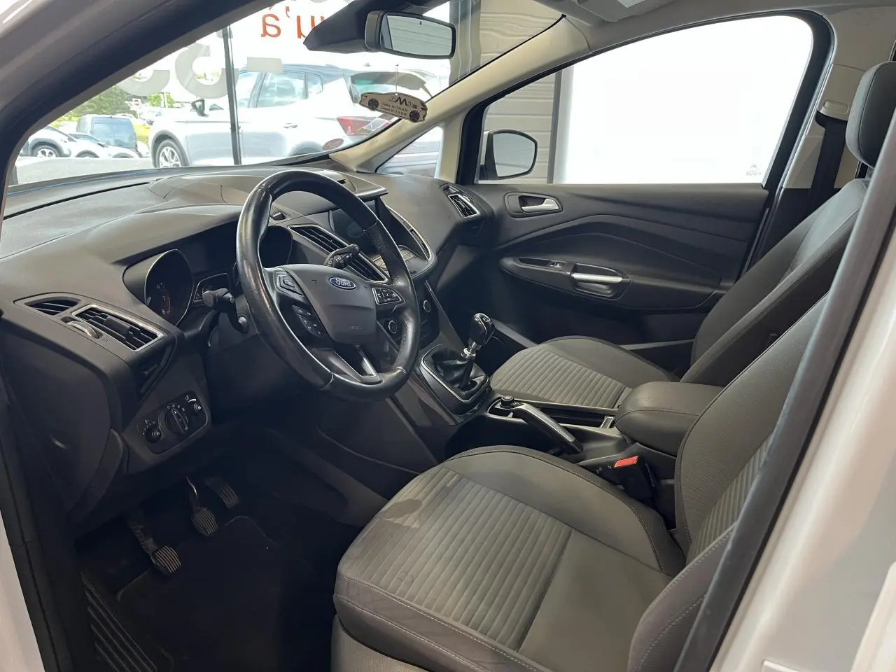 Intérieur avant gris d'une Ford C-MAX blanche 2018, vue côté conducteur avec volant cuir et boîte manuelle.