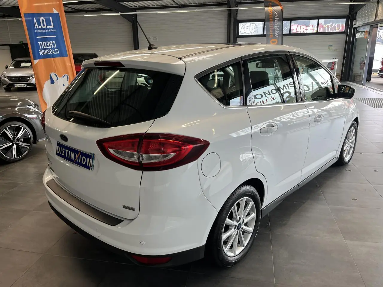 Vue 3/4 arrière droite d'un Ford C-MAX blanc en showroom avec jantes alliage et vitres teintées.