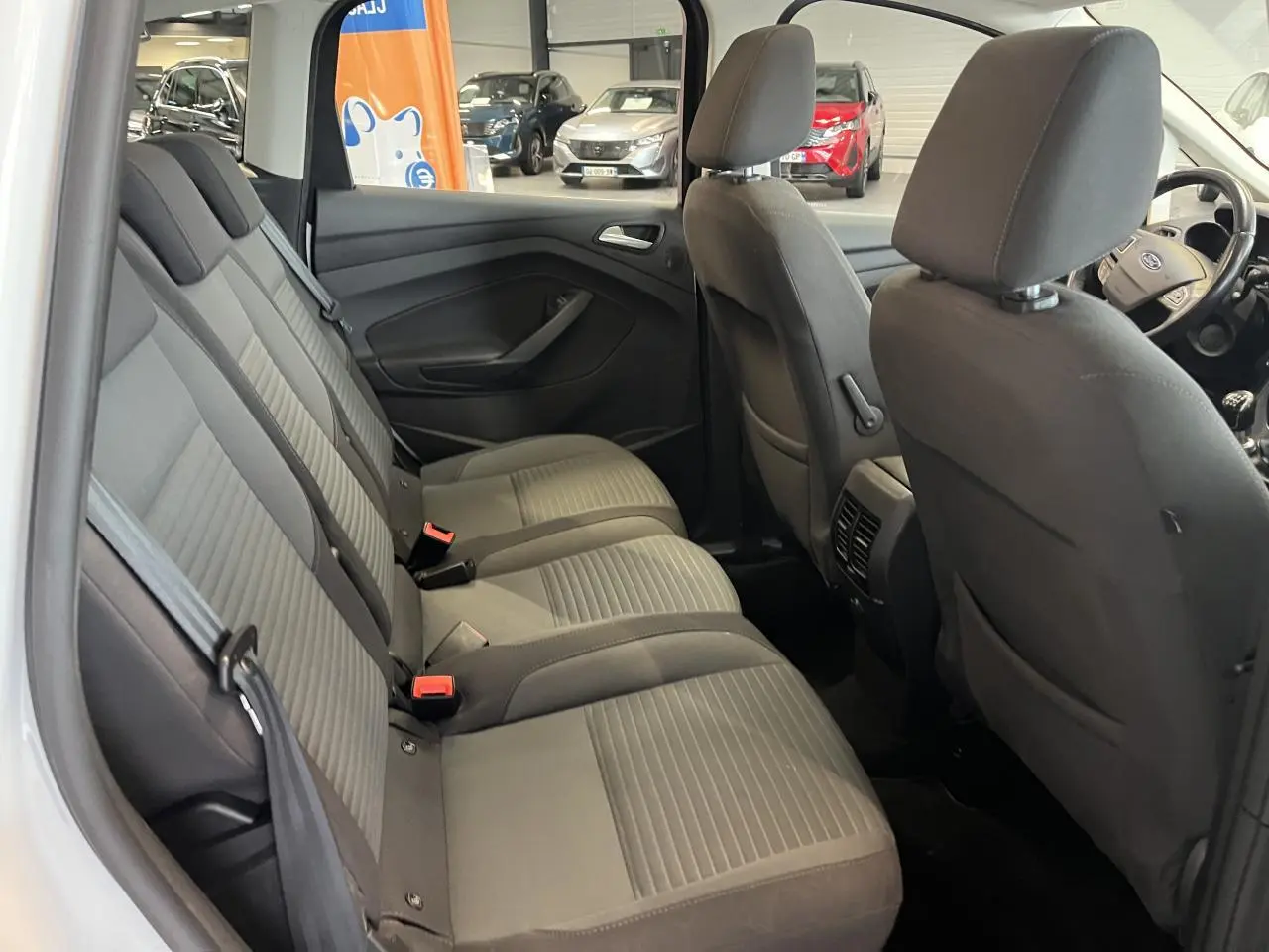 Vue intérieure côté droit des sièges arrière gris foncé du Ford C-MAX blanc, avec appuie-têtes et ceintures visibles.