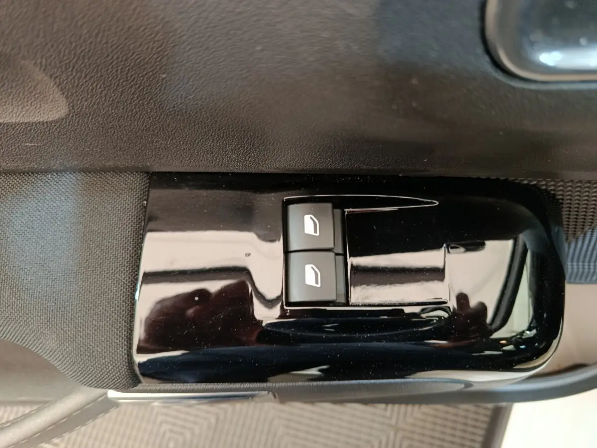 Gros plan sur les commandes de lève-vitres avant gauche d'une Citroën C3 blanche, finition intérieure noire brillante.