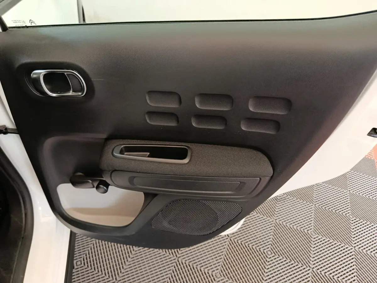 Vue rapprochée de la porte arrière droite noire de la Citroën C3 blanche, avec poignée et haut-parleur intégrés.