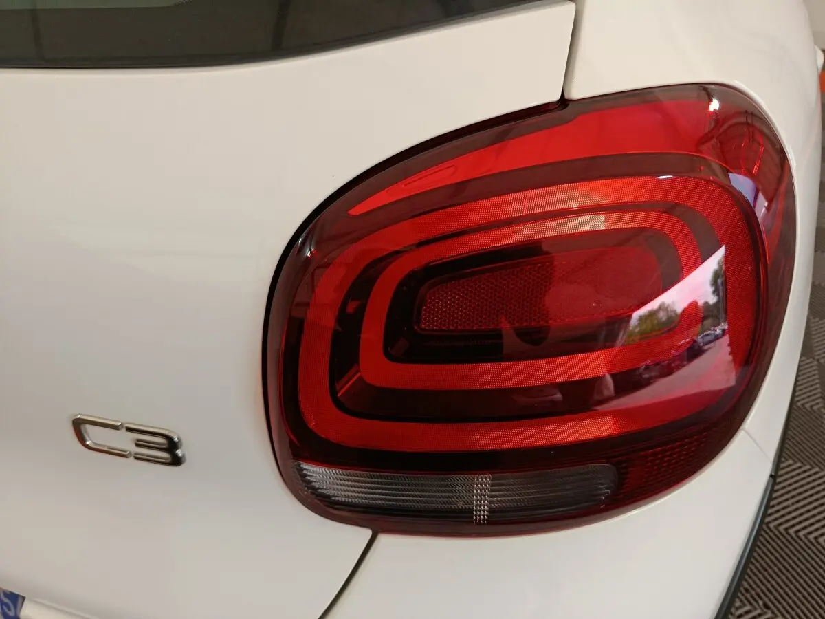 Gros plan sur le feu arrière droit rouge et le logo C3 d'une Citroën C3 blanche vue de l'arrière.