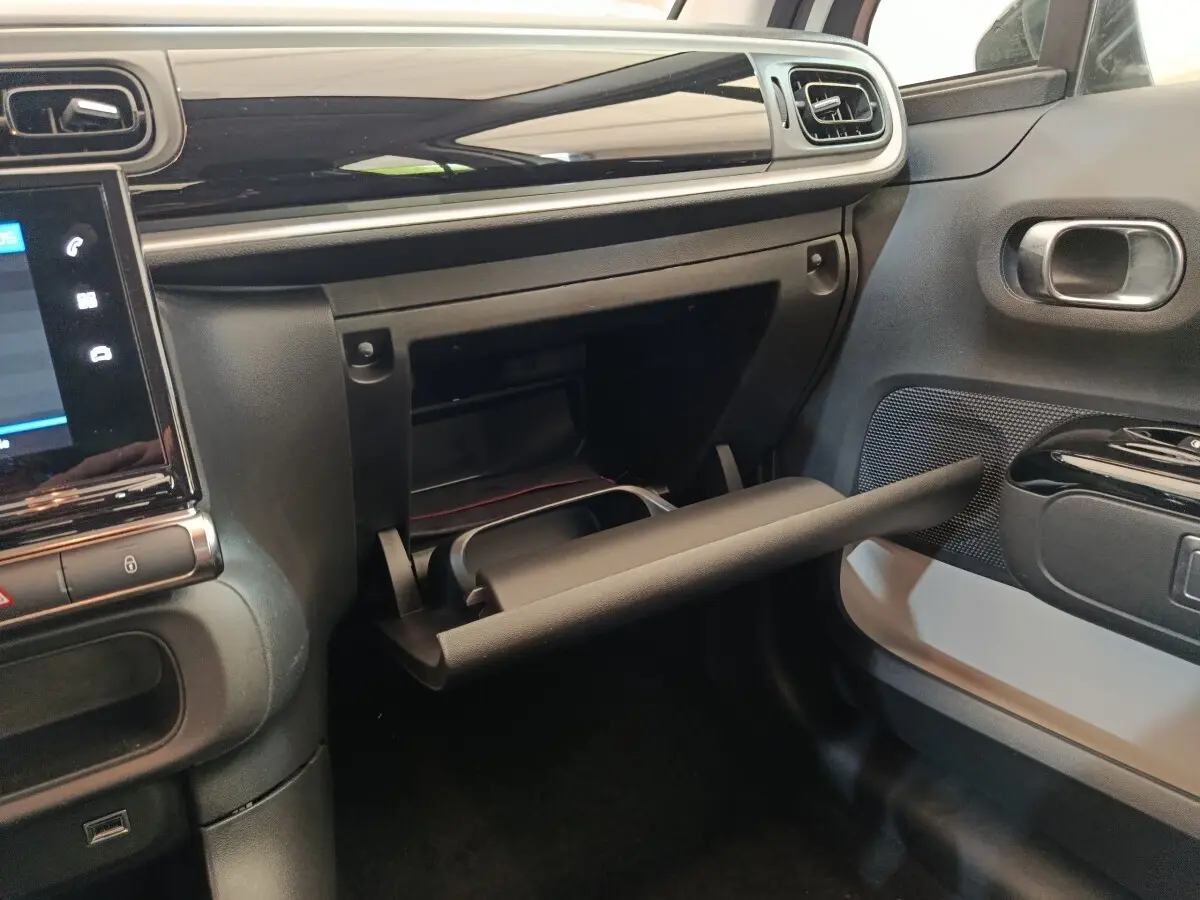 Vue intérieure côté passager du tableau de bord noir et gris avec boîte à gants ouverte d'une Citroën C3 blanche 2020.