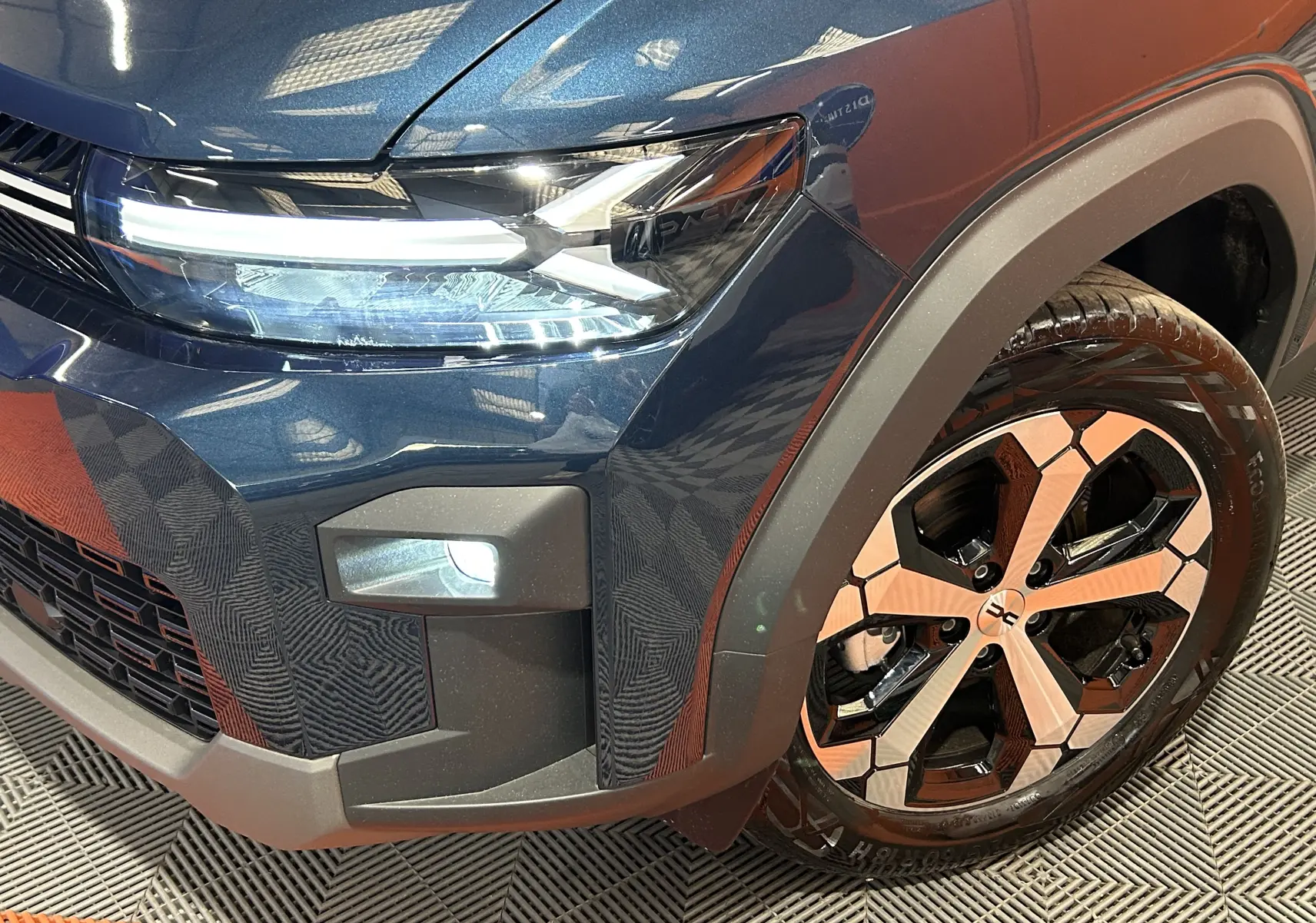 Gros plan sur l’avant droit bleu indigo du Dacia Bigster 2026, mettant en valeur le phare LED et la jante bicolore.