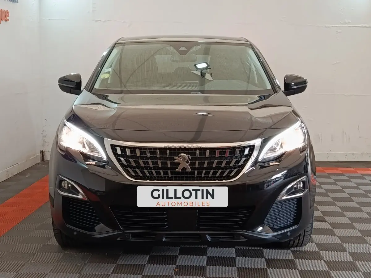 Vue frontale d’un Peugeot 5008 noir 2020 avec phares allumés et calandre chromée, en intérieur showroom.