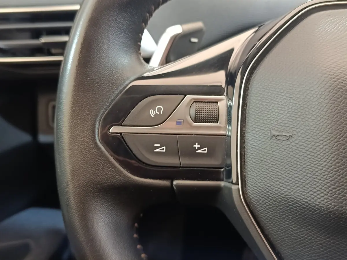 Gros plan sur les commandes gauche du volant cuir noir du Peugeot 5008, avec boutons de volume et reconnaissance vocale.