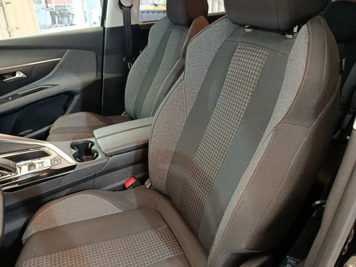 Vue intérieure rapprochée des sièges avant gris avec surpiqûres orange du Peugeot 5008 noir, version Active Business.