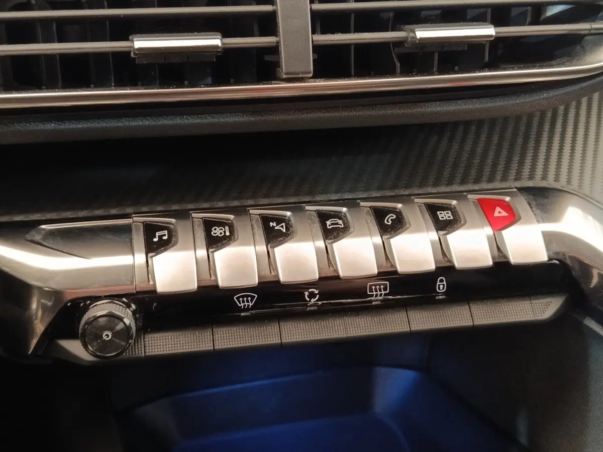 Gros plan sur la rangée de boutons métalliques du tableau de bord du Peugeot 5008 noir, avec bouton rouge d’alerte.