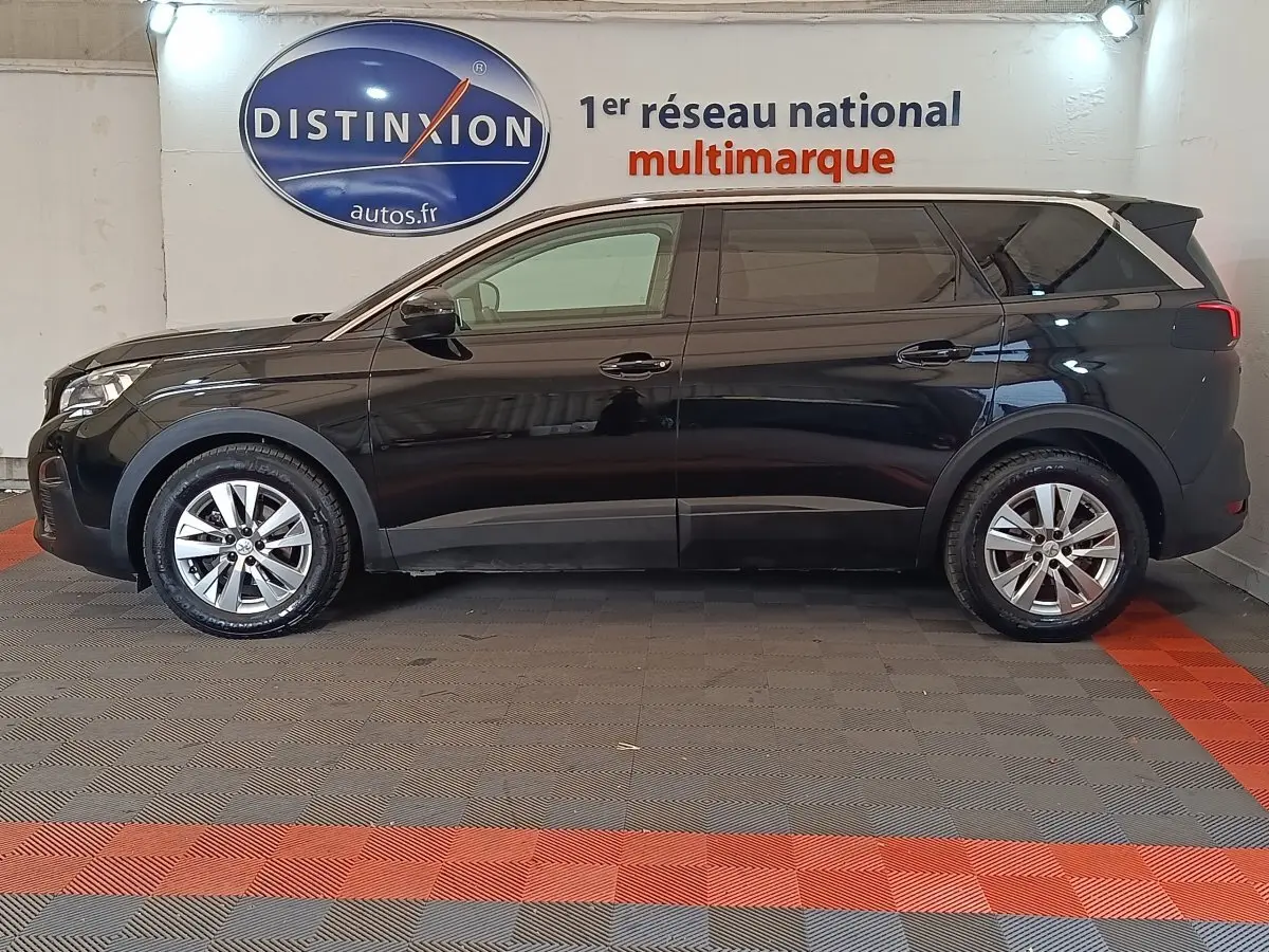 Vue de profil côté gauche d'un Peugeot 5008 noir 2020 garé en intérieur avec jantes alliage et vitres teintées.
