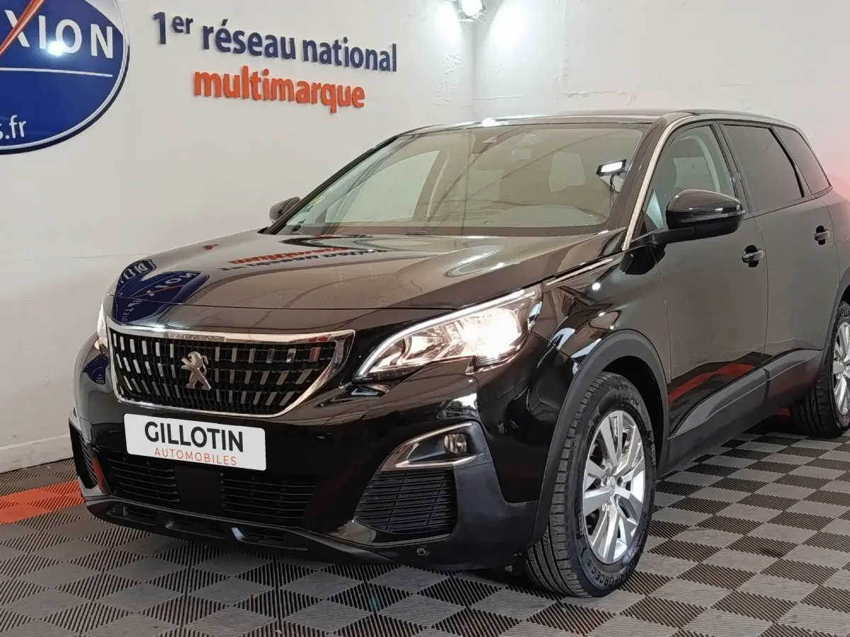 Peugeot 5008 noir vue 3/4 avant droit, avec calandre chromée et phares allumés en intérieur showroom.