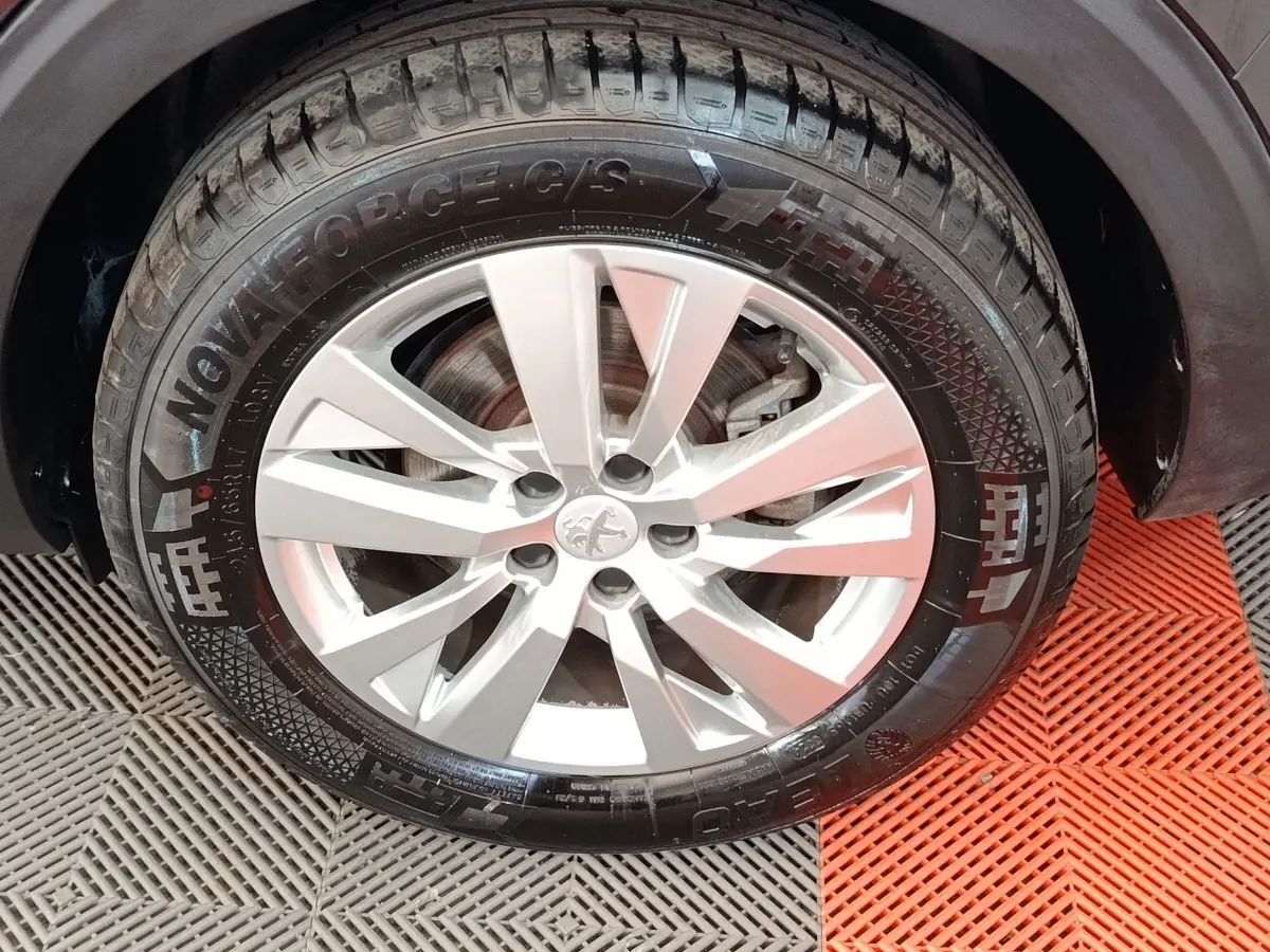 Gros plan sur la roue avant droite d’un Peugeot 5008 noir, jante alliage argentée à 5 doubles branches.