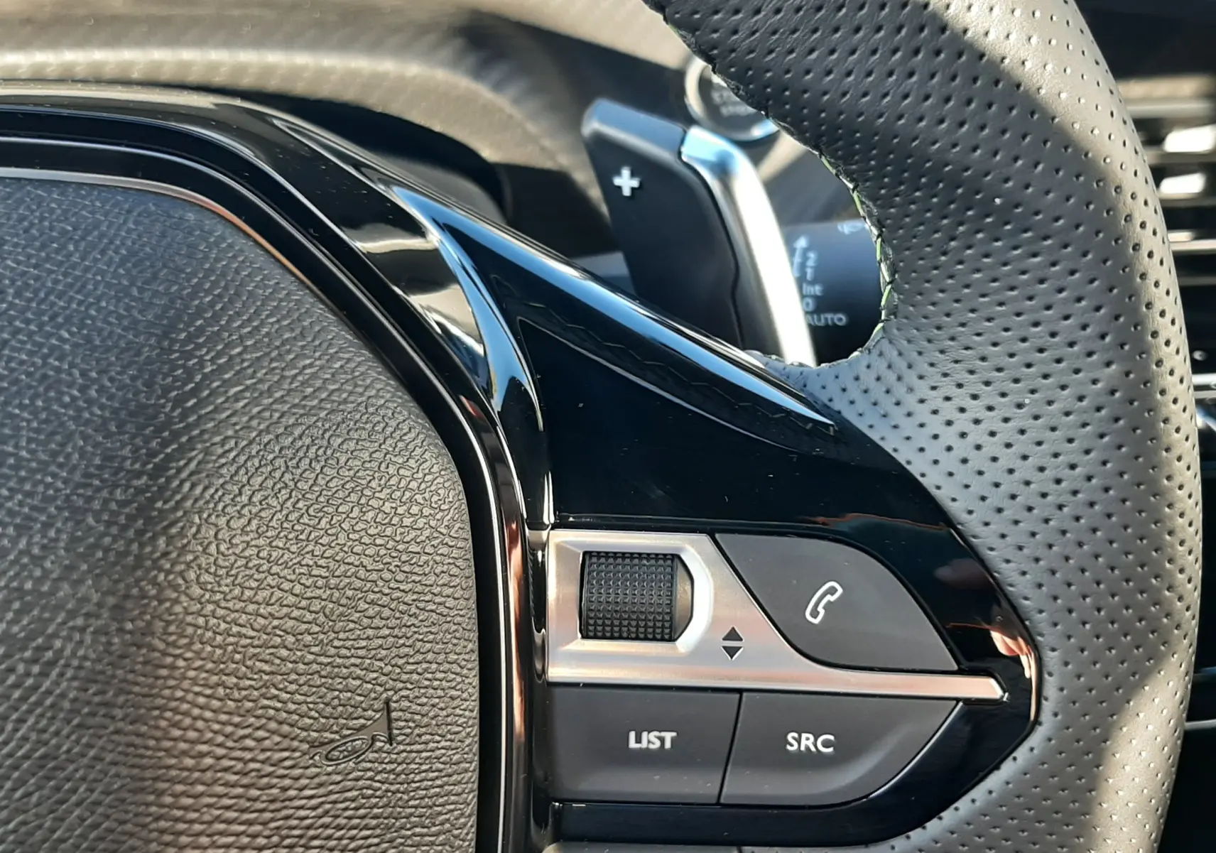 Gros plan sur la partie gauche du volant perforé du Peugeot 2008 gris, avec commandes audio et téléphone intégrées.