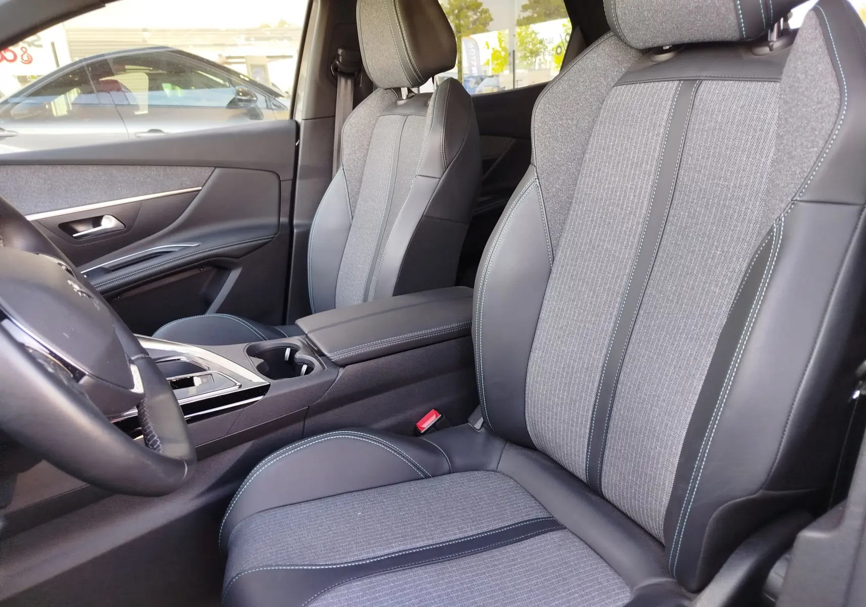 Vue intérieure côté conducteur du Peugeot 3008 2023, sièges tissu et cuir gris avec surpiqûres bleues.