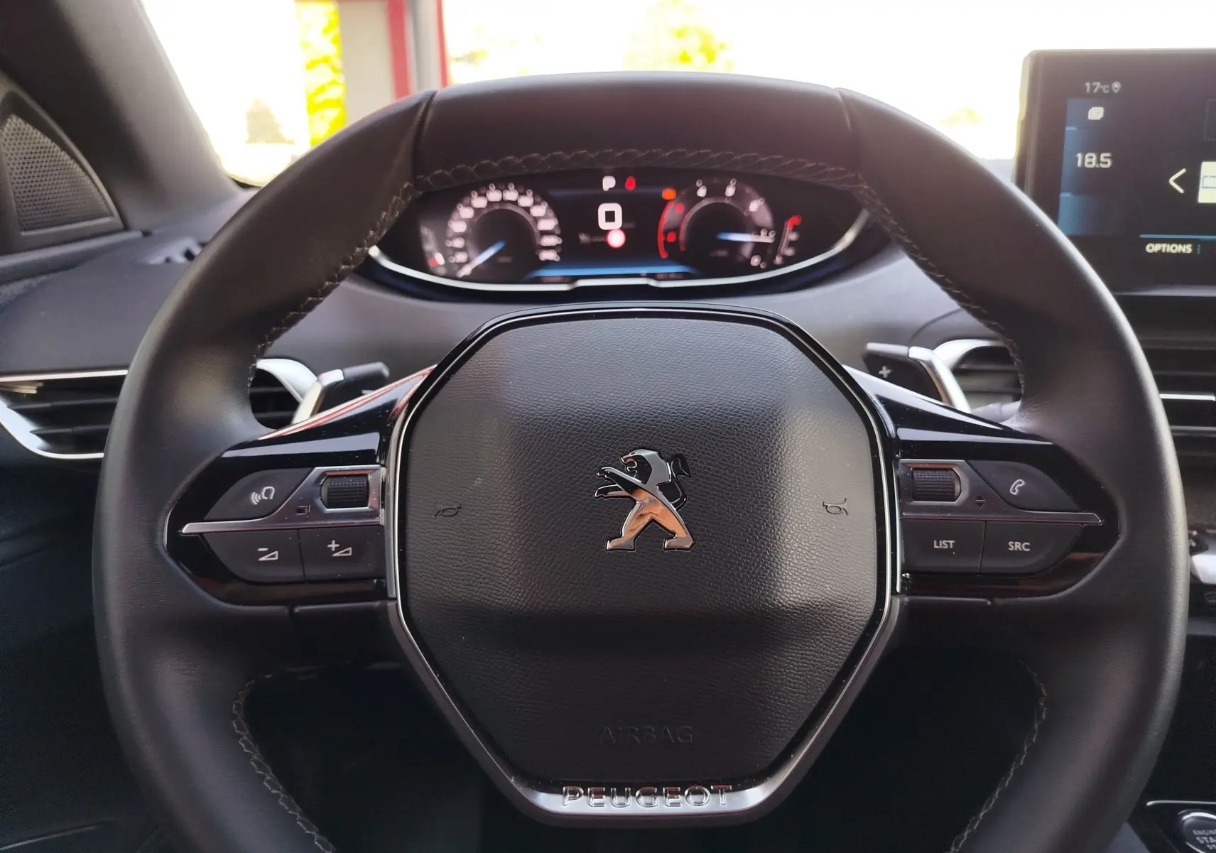 Gros plan sur le volant multifonction noir du Peugeot 3008 2023 avec tableau de bord numérique en arrière-plan.