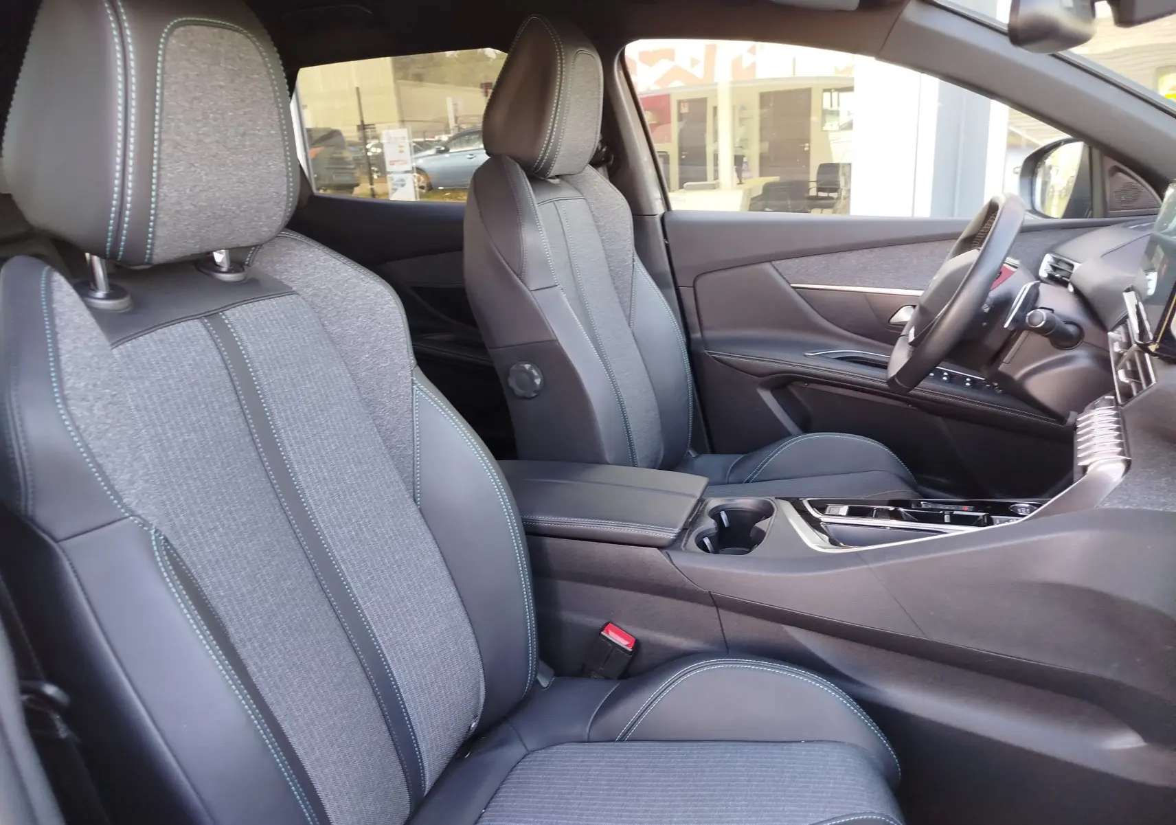 Vue intérieure côté droit du Peugeot 3008 2023, montrant les sièges bi-matière gris avec surpiqûres bleues et la console centrale moderne.
