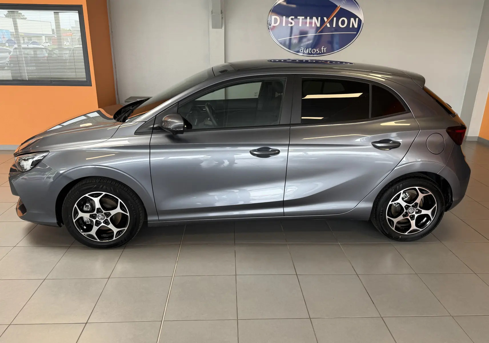 Vue latérale droite d'une MG3 hybride gris Hampstead avec jantes alliage et vitres surteintées en intérieur showroom.