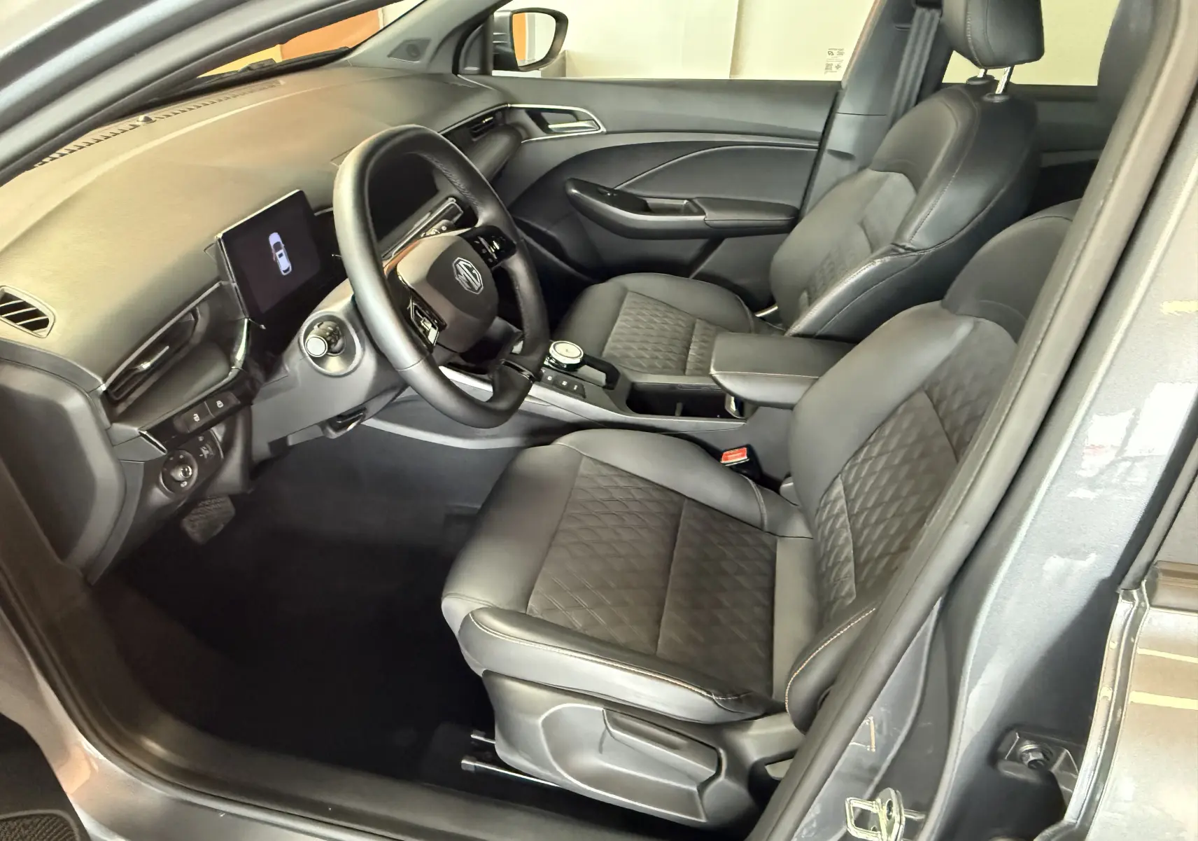 Vue intérieure côté conducteur du MG3 1.5 L Hybrid+ Luxury en gris Hampstead, avec sièges noirs en similicuir et volant cuir.