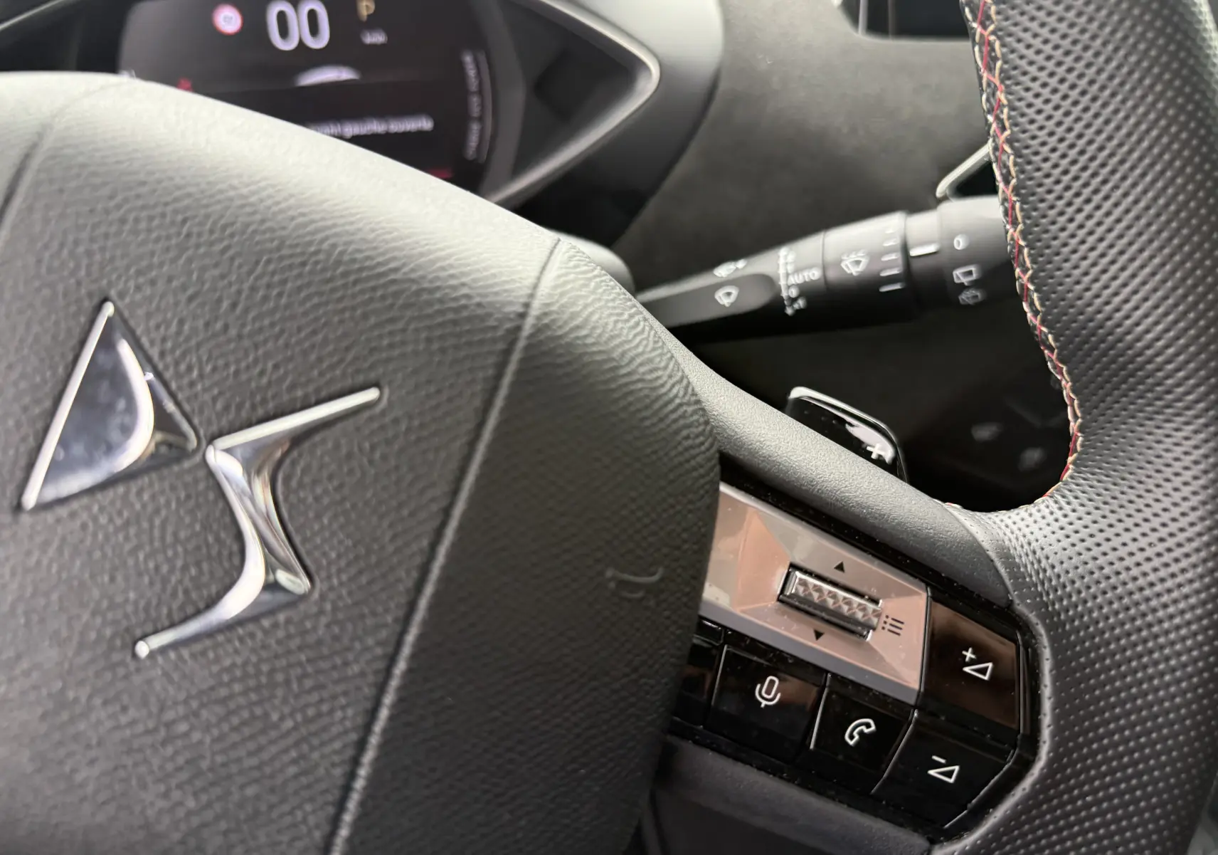 Gros plan sur le volant noir perforé du DS3 hybride 2025, avec commandes intégrées et logo DS argenté au centre.