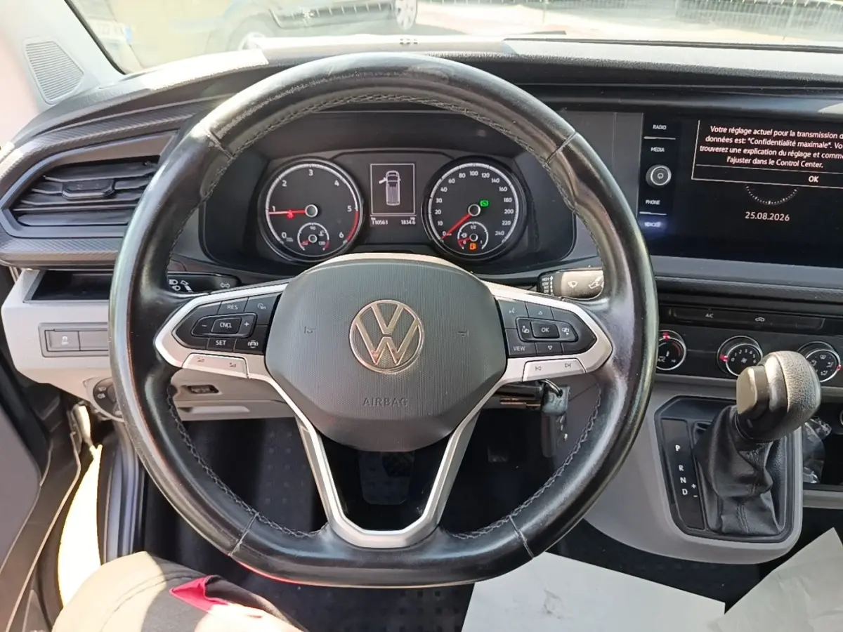 Vue intérieure centrée sur le volant cuir multifonctions et tableau de bord numérique du Volkswagen Transporter gris foncé.