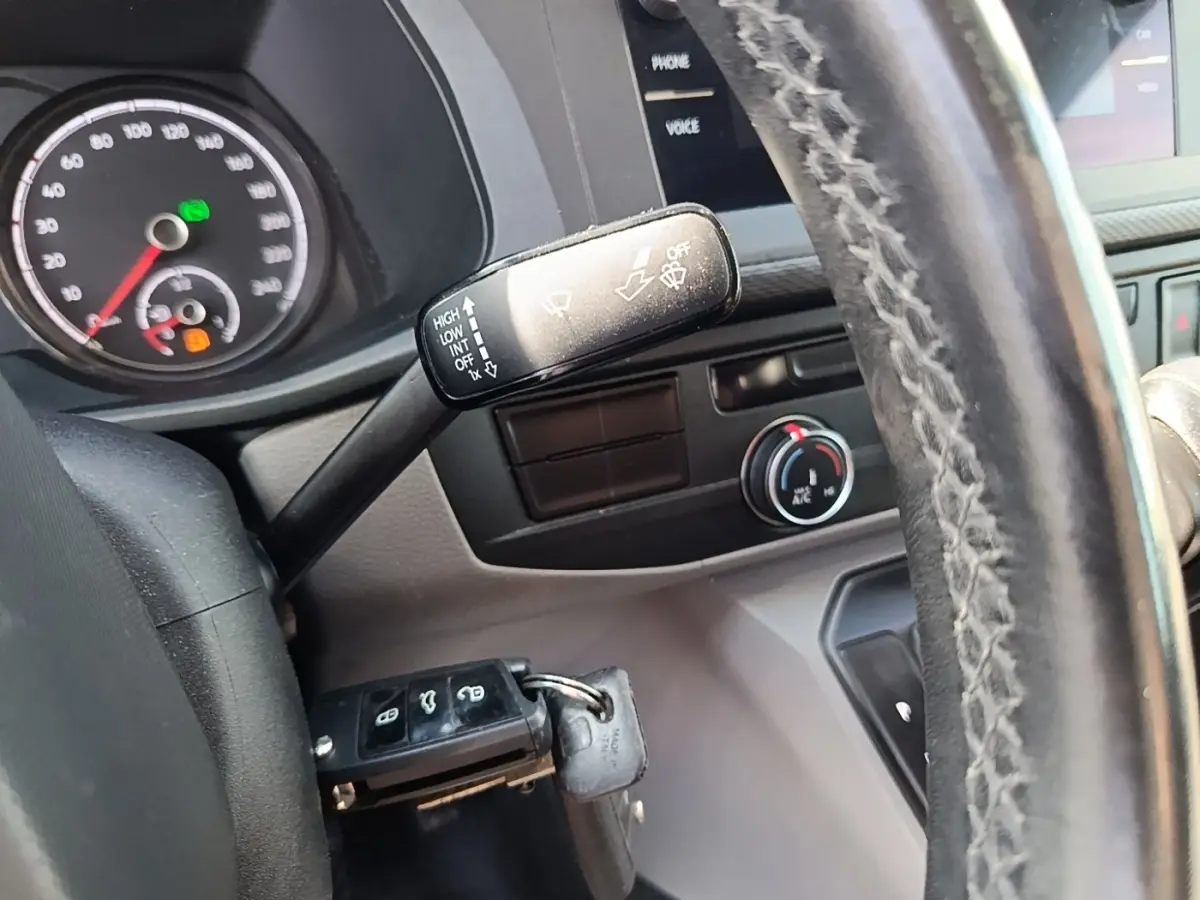 Gros plan sur le volant cuir et le commodo d’essuie-glace du Volkswagen Transporter gris foncé, tableau de bord partiel visible.