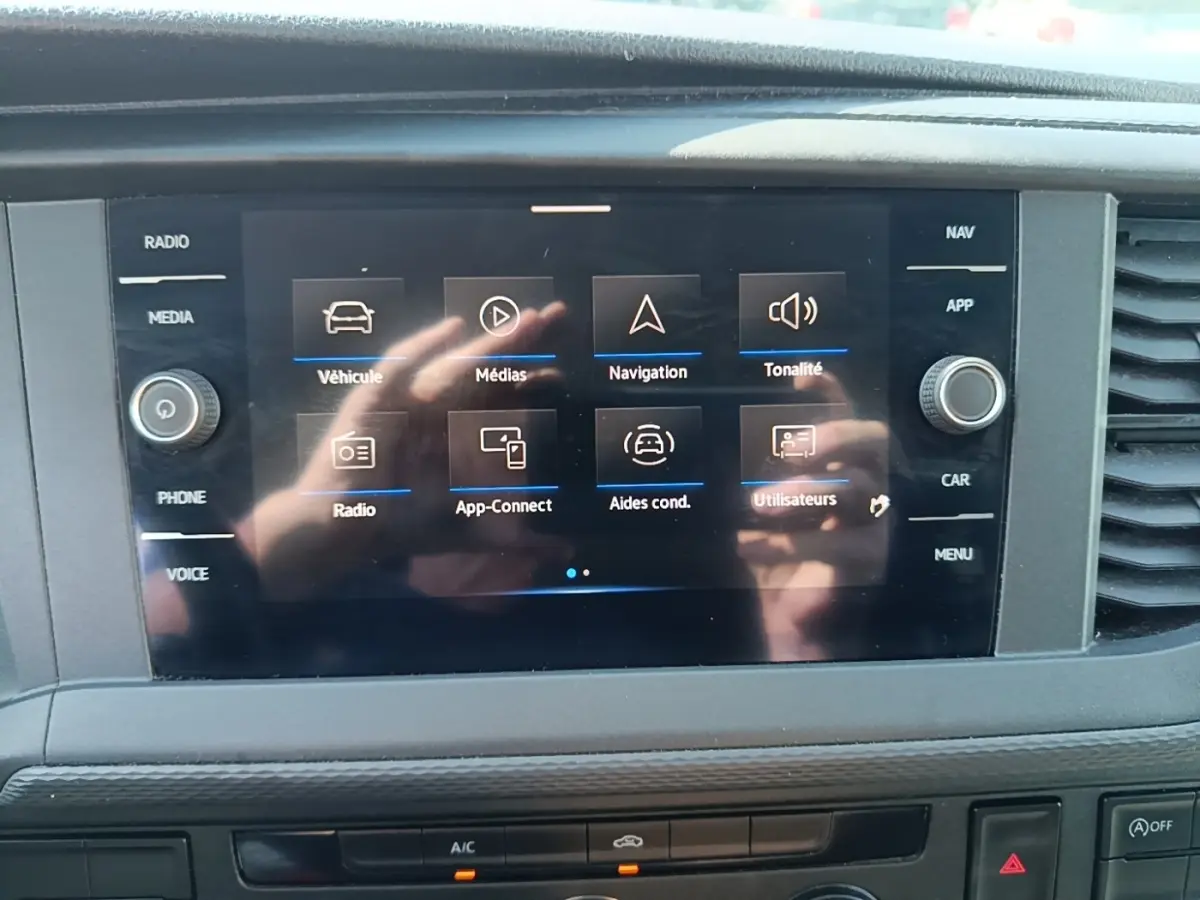 Écran tactile central du Volkswagen Transporter 2022 affichant les menus navigation et médias, avec reflets de mains.