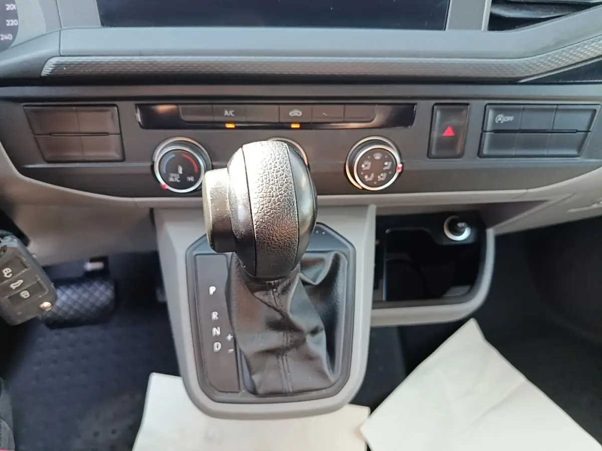 Gros plan sur le levier de vitesses automatique en cuir noir du Volkswagen Transporter gris foncé, tableau de bord en arrière-plan.