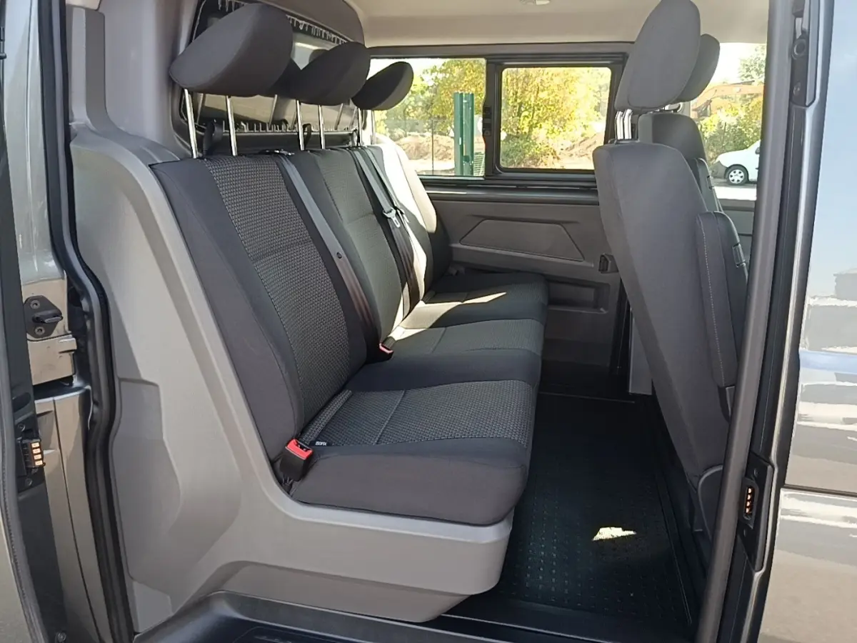 Vue intérieure côté gauche du Volkswagen Transporter gris foncé, montrant la banquette arrière trois places et la cloison vitrée.