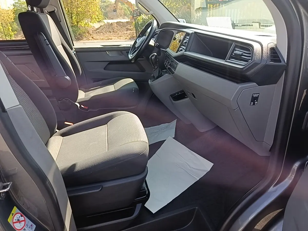 Vue intérieure côté conducteur du Volkswagen Transporter gris foncé, montrant sièges tissu et tableau de bord moderne.