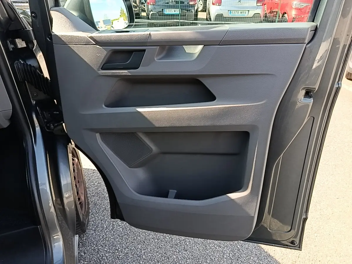 Vue rapprochée de la porte avant gauche ouverte d’un Volkswagen Transporter gris foncé, montrant le panneau intérieur en plastique gris.