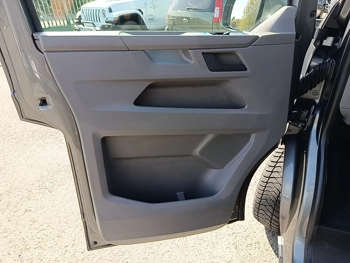 Vue rapprochée de la porte arrière droite ouverte d’un Volkswagen Transporter gris foncé, montrant le panneau intérieur en plastique gris.