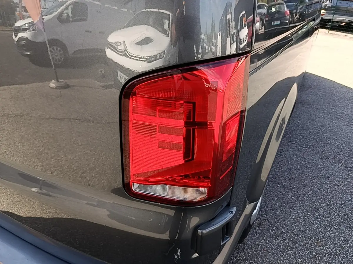 Gros plan sur le feu arrière droit du Volkswagen Transporter gris foncé, avec reflet de l’environnement urbain.