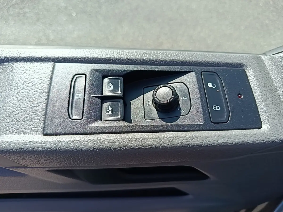 Gros plan sur les commandes de réglage des rétroviseurs et des vitres électriques côté conducteur du Volkswagen Transporter gris foncé.