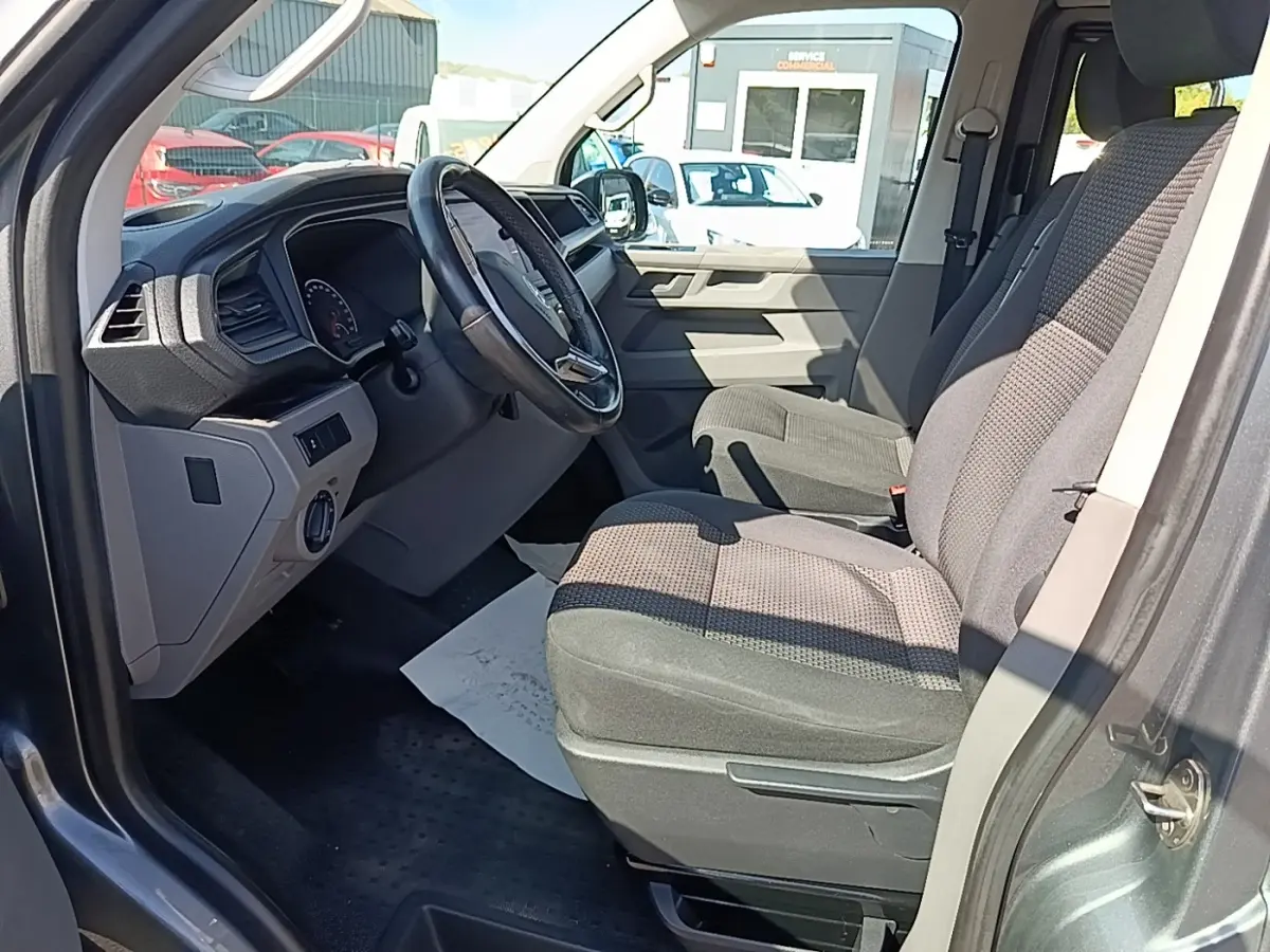 Vue intérieure côté conducteur du Volkswagen Transporter gris foncé, montrant le volant cuir multifonctions et les sièges tissu.