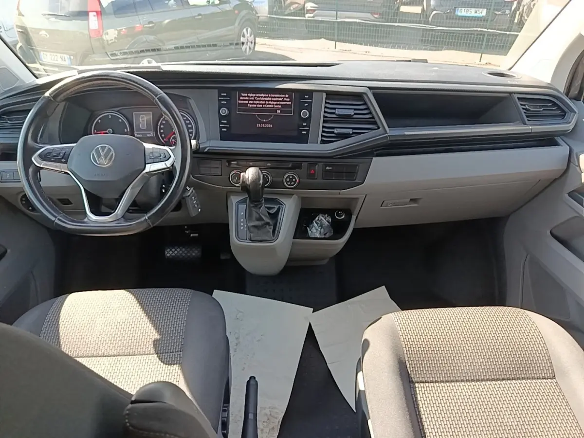 Vue intérieure avant du Volkswagen Transporter 2.0 TDi gris, tableau de bord avec écran tactile et volant multifonctions cuir.
