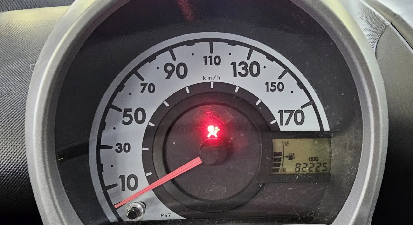 Gros plan sur le compteur de vitesse d'une Peugeot 107 jaune, affichant 82 225 km et voyant airbag allumé.