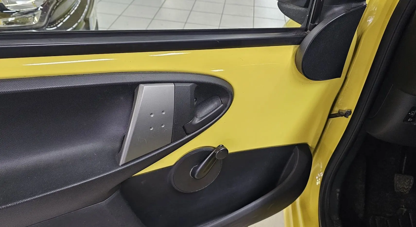 Intérieur de la porte avant gauche jaune d'une Peugeot 107 2013, avec poignée manuelle de vitre et panneau noir texturé.