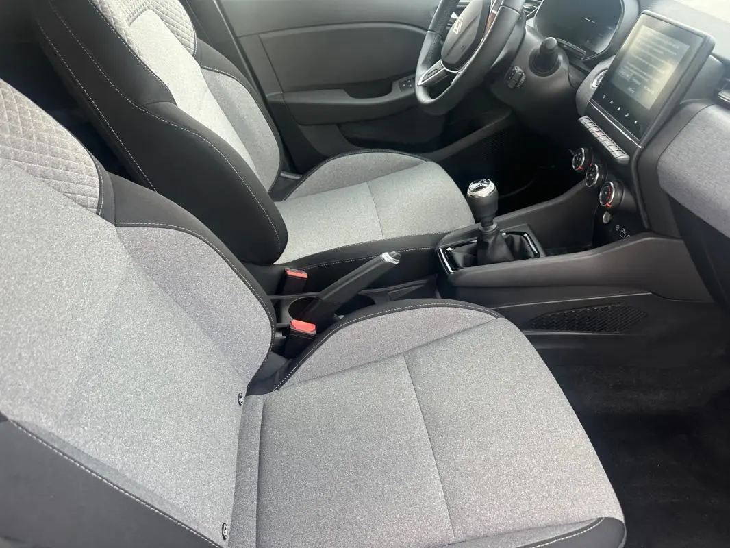 Vue intérieure côté conducteur de la Renault Clio V dCi 100 Evolution 2025, sièges gris et console centrale avec boîte manuelle.