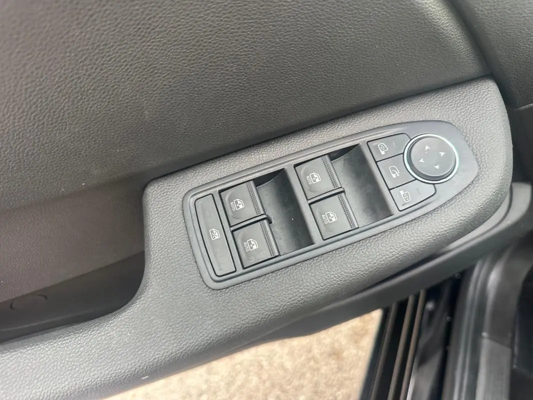 Gros plan sur les commandes des vitres électriques et des rétroviseurs sur la porte côté conducteur d’une Renault Clio noire.