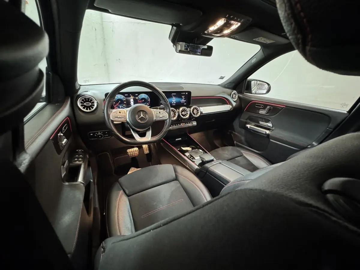 Vue intérieure avant du Mercedes GLB 200 d AMG Line noir, tableau de bord digital et éclairage d'ambiance rouge.