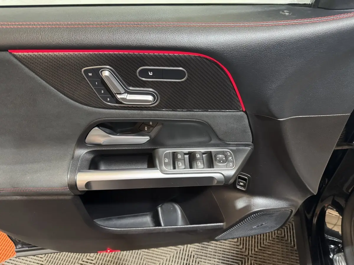 Gros plan sur la porte avant gauche noire du Mercedes GLB 200 d AMG Line avec commandes de sièges et bande rouge décorative.